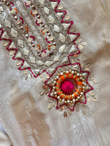 Festive cream dress material with neck embroidery, soft tissue fabric and decorative pom pom latkans