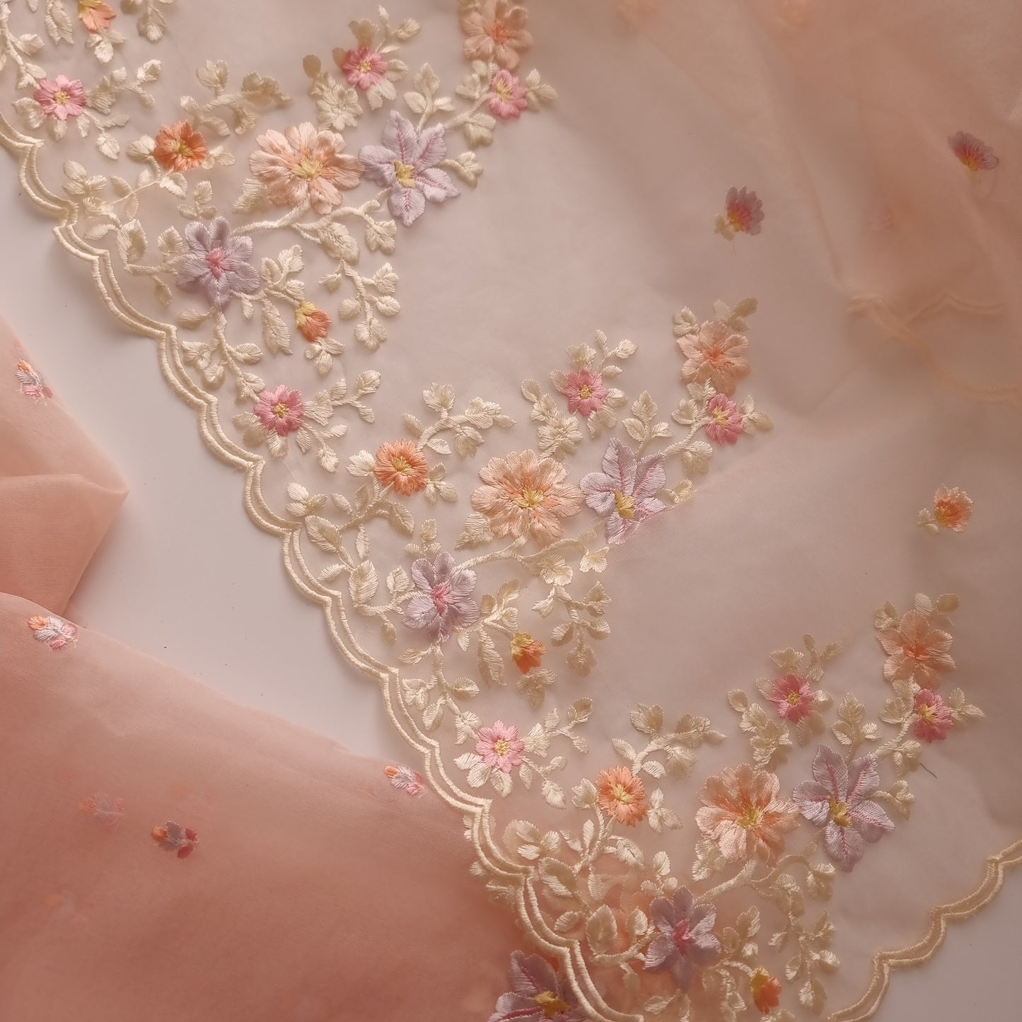 Detailed close-up of multicolor floral Parsi work embroidery on peach tissue fabric